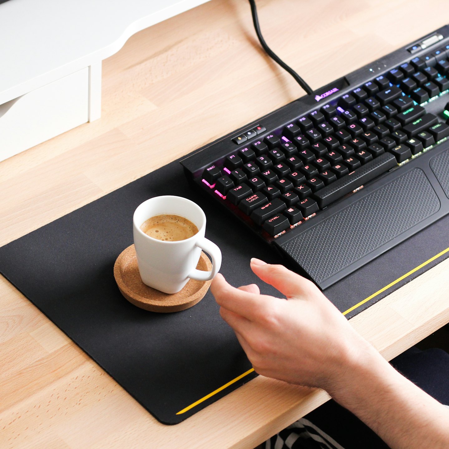 A hand rests near a coffee mug and mechanical keyboard.