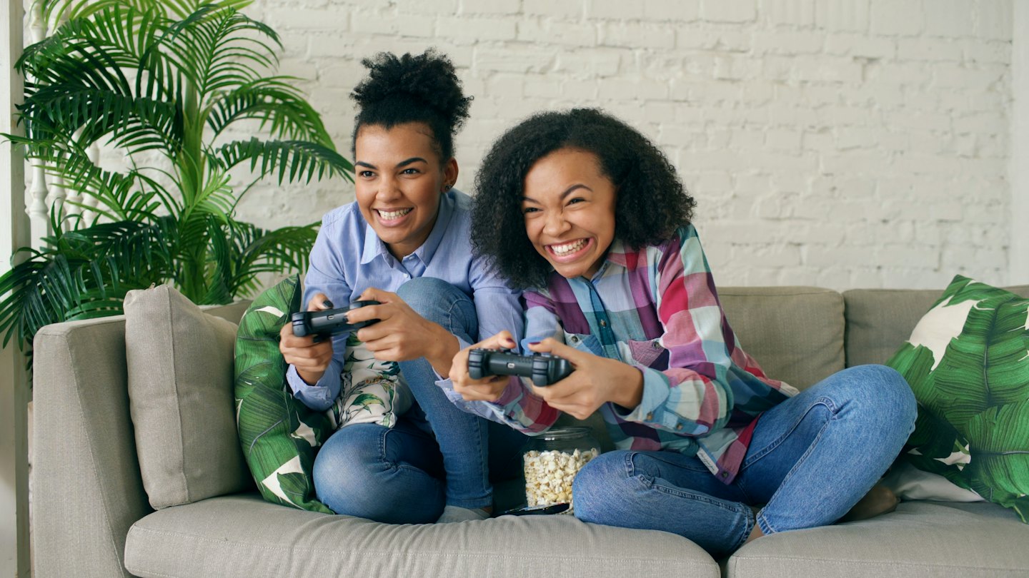 Two women laugh while playing video games with popcorn.