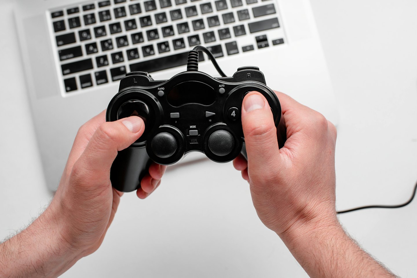 Hands holding a game controller over a silver laptop keyboard.